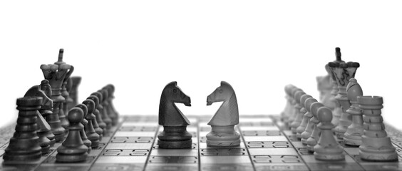 Black and white chess faceoff of both knight horses on top of a chess board in front of a white...