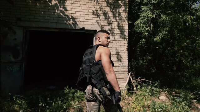 Brutal militant in khaki pants patrolling the area looks around incredulously and walks into the darkness of the brick building