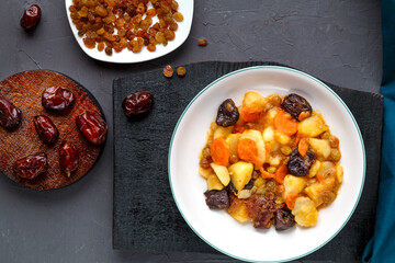 Jewish cuisine dish sweet tsimes with carrots vegetarian dates in a plate on a concrete background near dates raisins.