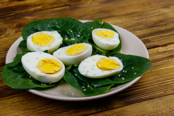 Boiled eggs with fresh spinach leaves and sesame seeds on wooden table