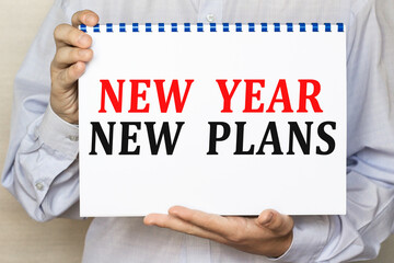 The businessman shows a sheet with the text NEW YEAR NEW PLANS on a white background. Business concept