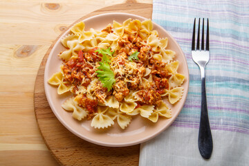 Pasta in tomato bolognese sauce in a plate on a wooden table on a napkin next to a fork
