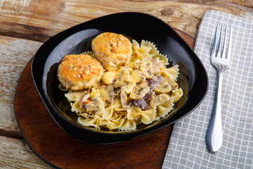 Pasta in a creamy sauce with mushrooms and chicken meatballs in a black plate on a napkin next to a fork.