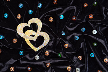 Two shiny gold hearts and multicolored glass balls on a black background. Valentine's day concept.