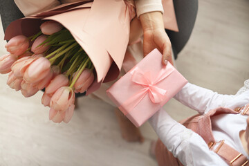 Child's hands hold beautiful pink gift box with ribbon and pink tulip flower. Top view, close-up....