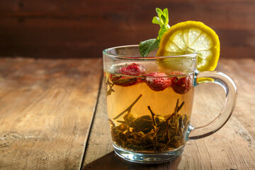 green tea in a glass cup with strawberries mint and lemon on a wooden table.