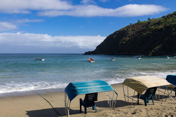 Beach awnings overlooking some boats in the turquoise sea of gentle waves with mountains and blue sky in the background in Chichiriviche de la Costa, Vargas Venezuela