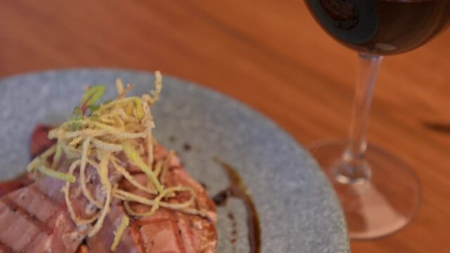 Tuna fillet on a parrilla with rostized jitomate in marmol plate. Tuna fillet and red wine glass