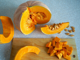 part of a bright orange pumpkin and sliced slices on a wooden board on the kitchen table in the sun