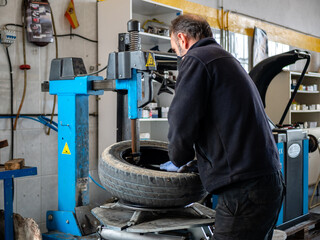 MECHANIC IN HIS WORKSHOP FIXING CAR WHEEL IN MACHINE