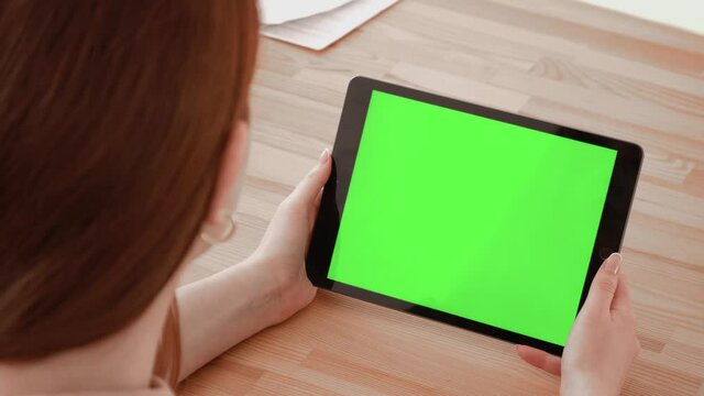 Close up shot of hands holding a tablet computer with green mock up screen. A template for video conference or online store