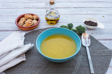 Healthy homemade vegetable creamy soup fresh and ready to eat. Made with carrots, potatoes, peas, celery and broccoli. On the wooden table, olive oil, black pepper and croutons