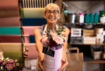 Portrait of senior woman in flower shop holding bouquet.