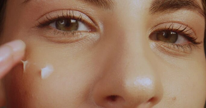 Macro shot cropped close-up of female face. Young woman gently applying moisturising cream under eyes.
