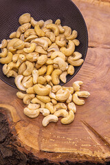 cashew nuts are poured from a dark cup onto a wooden background