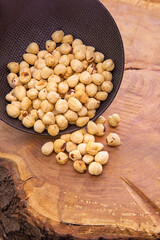 the kernels of the peeled, shell-less hazelnuts fall from a dark cup on a wooden background.