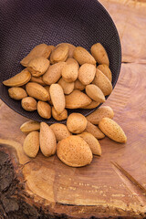 Krachmandeln.Unpeeled almond seeds fall from a dark cup on a wooden background.