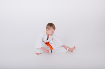 little boy in a white kimono with an orange belt does a warm-up on a white background with space for text