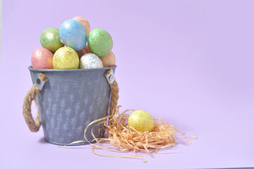 Colorful Easter eggs on a soft purple background in a gray bucket in the style of minimalism. with place for text. Easter background. High quality photo.