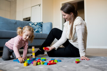 Naklejka premium Mother and daughter playing wooden cubes on the floor of the living room at home. Activities with children inside, early childhood development