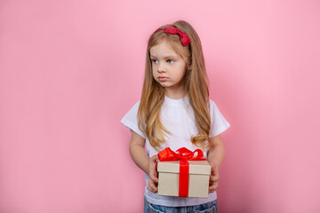 Little girl with a gift in a box standing on a pink background