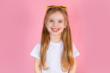 Little girl wearing sunglasses with long hair standing on a pink background with a big smile