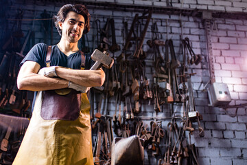 Authentic blacksmith man forges a metal product in dark indoors studio