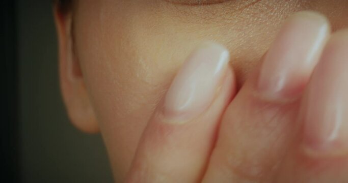 Macro shot cropped view of female face. Young woman gently applying moisturising cream on cheeks and under eyes.