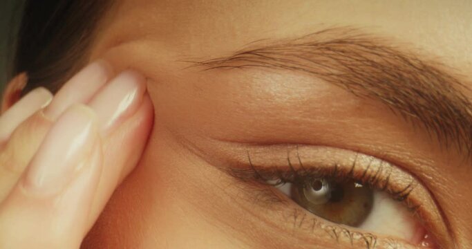 Macro shot cropped view of female face. Unrecognizable woman gently massaging applying moisturising cream on cheeks and under eyes.