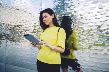 Pensive asian woman in casual wear standing outdoors reading news and notification on digital tablet, serious influencer hipster girl 20s watching video via touchpad and 4G internet connection