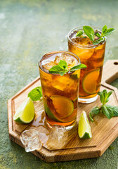 Refreshing drink, iced tea with lime wedges in glasses on a wooden board on a green concrete background. Summer drinks.