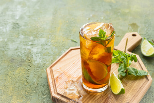 Refreshing drink, iced tea with lime wedges in glasses on a wooden board on a green concrete background. Summer drinks.