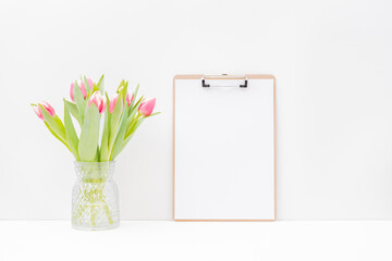 Home interior with easter decor. Mockup with a clipboard and pink tulips in a vase on a light background