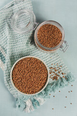 Organic uncooked scattered buckwheat grain in a bowl and glass jar on a light blue background