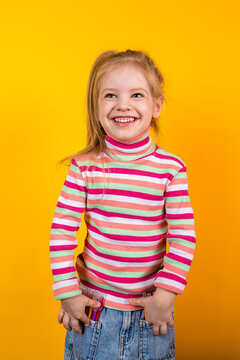Young girl artist in a striped sweater standing on a yellow background with felt-tip pens in jeans pockets, vertical photo