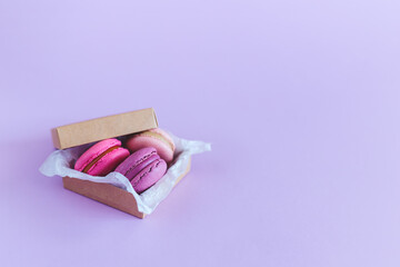 Tasty french macarons in a box on a violet pastel background. Pink and violet macarons.