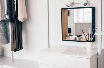 women's wardrobe with stylish clothes on hangers in a bright interior and a boudoir table