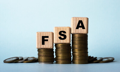 FSA - acronym on wooden cubes. Which stand on stacks of coins on a light background