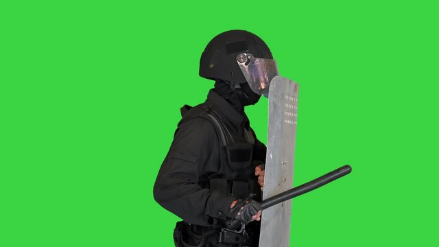 Policeman with full equipment for anti-riot standing covering with a shield holding position on a Green Screen, Chroma Key.