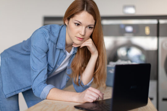 young woman using a laptop in a launderette - Powered by Adobe