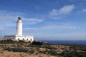 Fototapeta na wymiar Faro de Cabo Salinas (Mallorca) con cielo azul ligeramente salpicado de nubes.