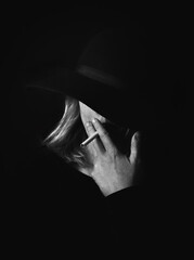 woman with her face covered by a hat smoking a cigarette in B&W
