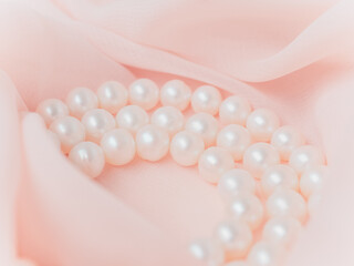 Women wedding jewelry. Necklace of natural pearls on pink gentle chiffon fabric as background....