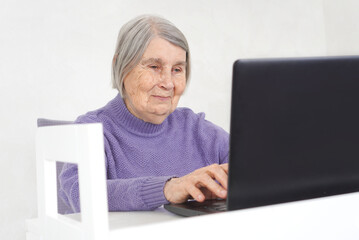 Smiling elderly woman working on a laptop. Portrait of cheerful old lady surfing internet.