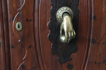 Aldaba con figura de mano sosteniendo una bola, en una puerta de madera noble marrón oscuro.
