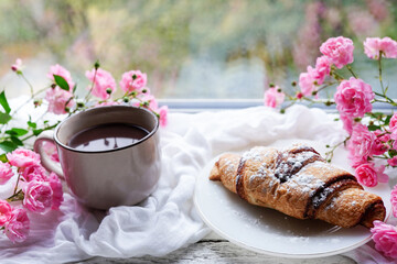 breakfast - delicious fresh croissant with coffee cup and pink roses on the window sill