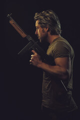 Fototapeta premium Rugged man with gun in green t-shirt against dark background.