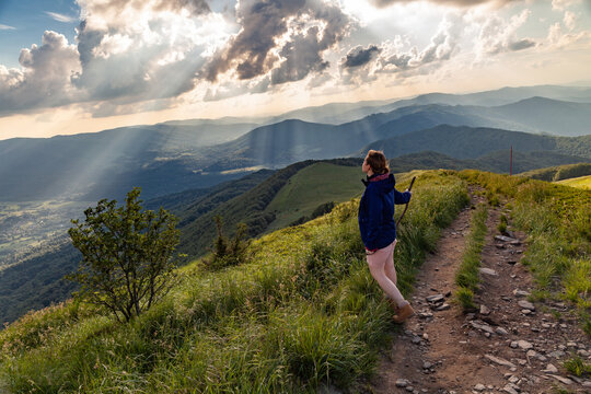 Turystka podziwia promienie światła oświetlające dolinę, w kt&oacute;rej znajduje się g&oacute;rska wieś Wetlina, Bieszczady, Polska