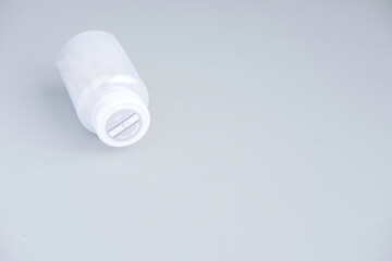 White plastic  jar with viatmins with a sticker on the lid with inscription non-gmo 100% vegan lies on a gray background on the left of the frame