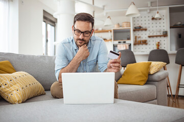 Handsome man with laptop and credit card at home, portrait. Shot of a handsome young businessman...